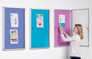 3 different coloured noticeboards and a woman pinning a poster to one